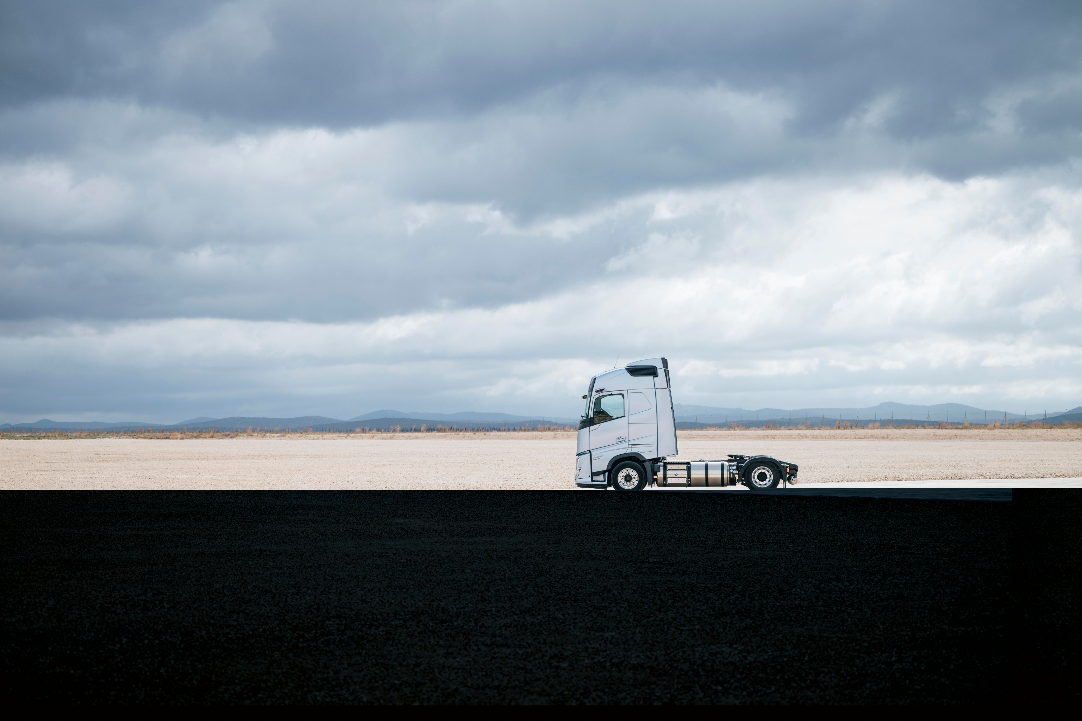 Vista lateral de um camião Volvo estacionado numa paisagem ampla e aberta sob um céu nublado, com arredores vastos e cenário minimalista.